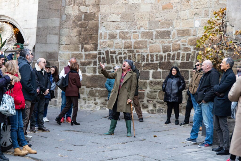 Il pubblico della passeggiata-racconto ascolta un attore in costume tra le mura di pietra di Viterbo